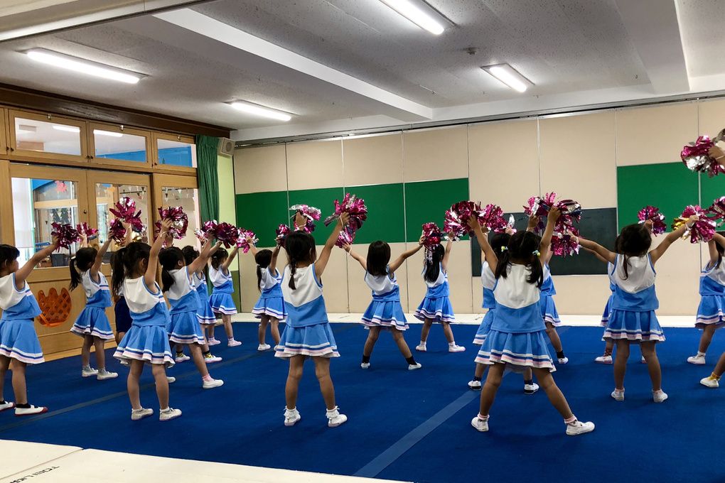 体育館で、ポンポンを高く上げる子どもたちの後ろ姿