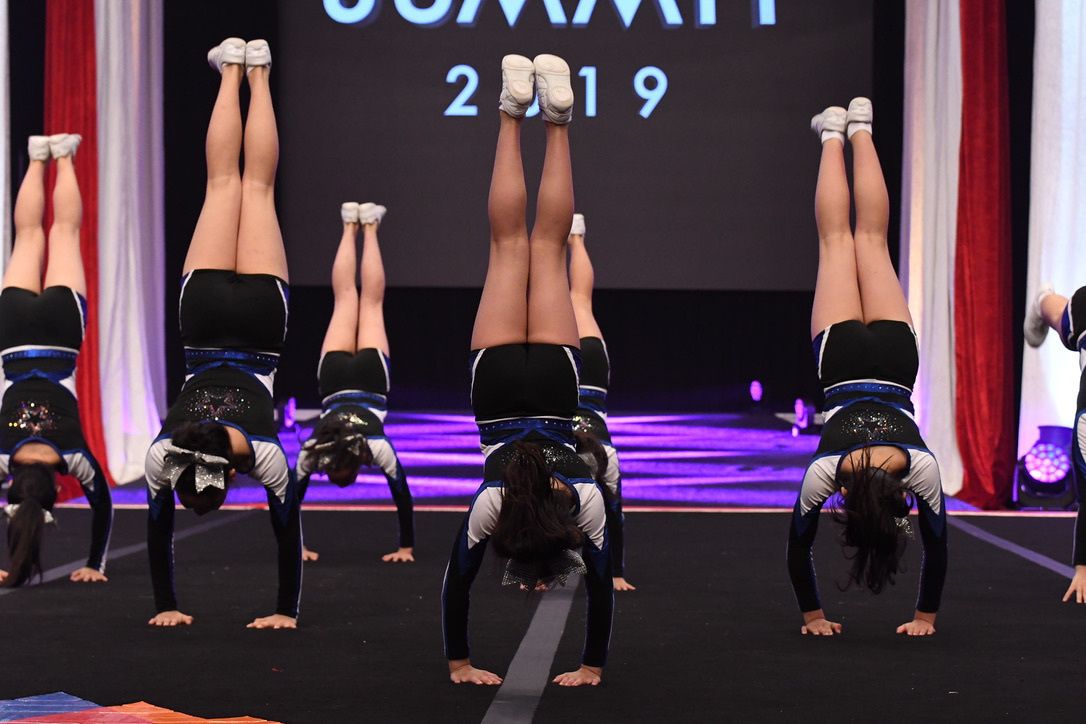 The SUMMIT 2019 のステージで、黒いユニフォームのチームが逆立ちをしている様子